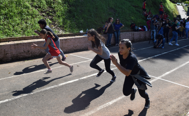Em uma pista de corrida, quatro crianças em uma largada saem correndo