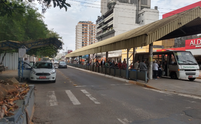 Rua com um carro parado e uma parada de ônibus à direita