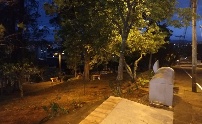 Imagem de uma praça com arvores e grama iluminada