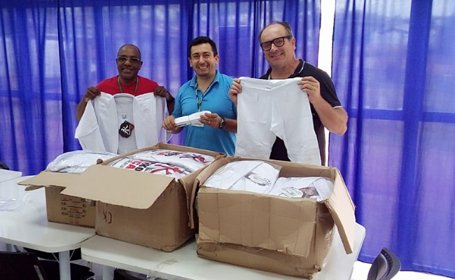 Três homens em pé, atrás de uma mesa, mostrando os quimonos, que estão dentro de uma caixa em cima da mesa