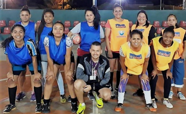 Grupo de mulheres e um homem, sendo que ele está agachado. As mulheres vestem coletes azuis e amarelos