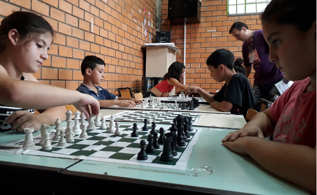 Em uma mesa, crianças jogam xadrez