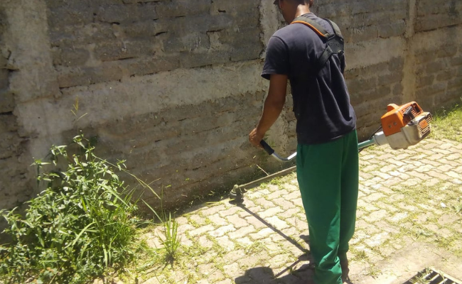 Homem de costas com um cortador de grama executando o serviço