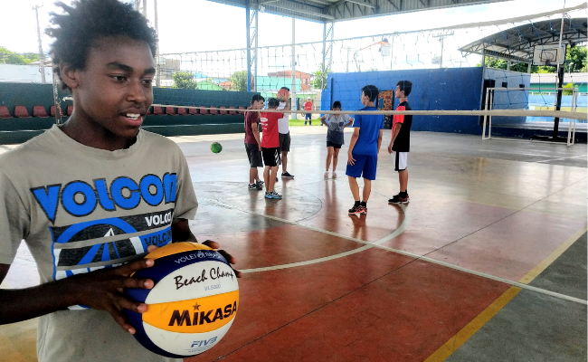 Menino em pé em uma quadra de vôlei segurando uma bola