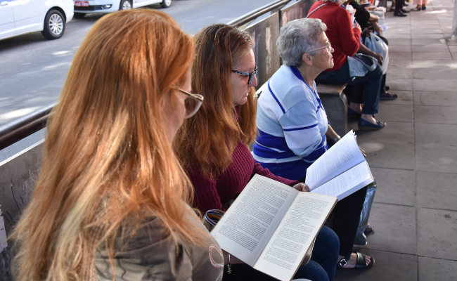 Em uma parada de ônibus, duas mulheres sentadas leem segurando livros nas mãos