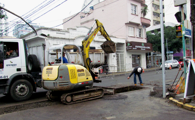 Máquina cavando um buraco em uma esquina. Um homem mede este buraco com um fita