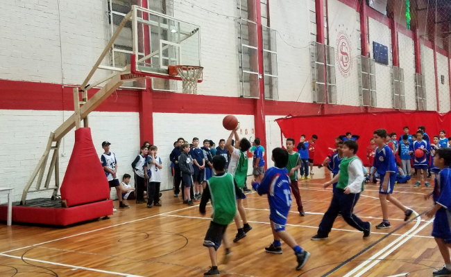 Em uma quadra de basquete, meninos jogam, com um deles fazendo um arremesso na cesta