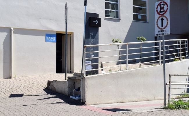 Prédio de concreto com uma porta. Ao lado da porta, uma placa azul escrita SAME
