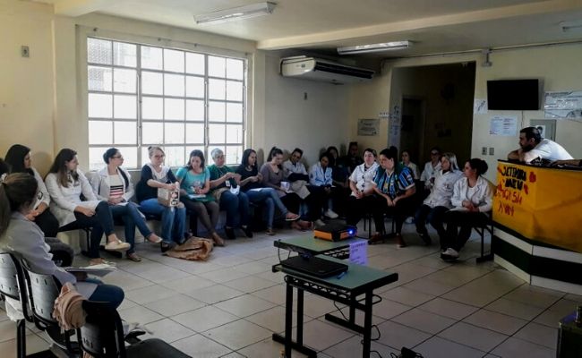 Em uma unidade de saúde, pessoas sentadas em cadeiras em formato de semicírculo