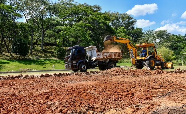 Em uma grande área, uma retroescavadeira retira terra e coloca em uma caminhão